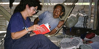 Eine Frau sitzt mit einem Buch auf dem Boden und unterhält sich mit einem Mann, der in einer Hängematte liegt